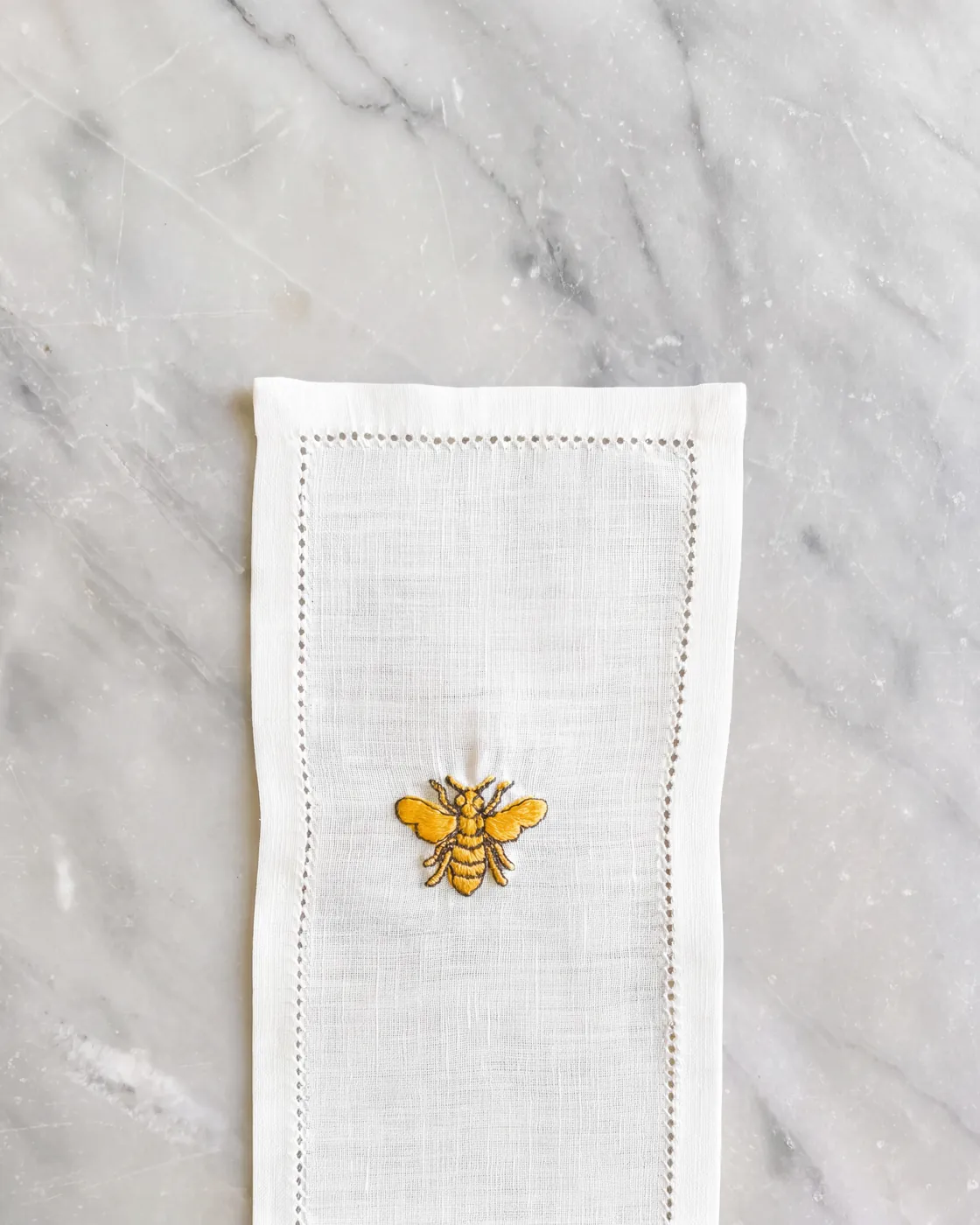 A linen napkin embroidered with a golden bee, on marble
