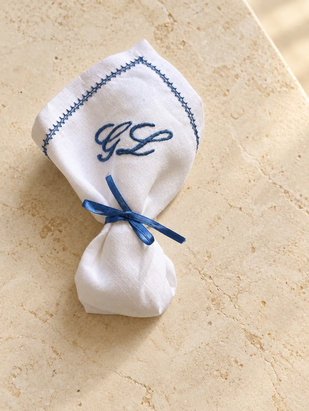 Square white linen napkin with blue initials, tied with a blue ribbon